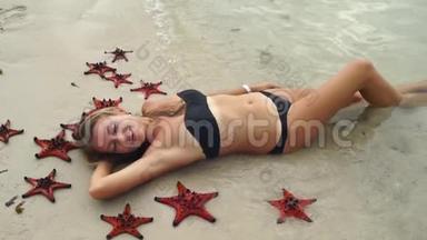 一个年轻美丽的女人躺在海滩上，被红色的星星鱼包围着